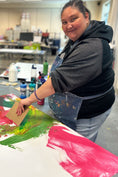 Load image into Gallery viewer, Artist Jamie N. looking up from from her work on painting a large canvas